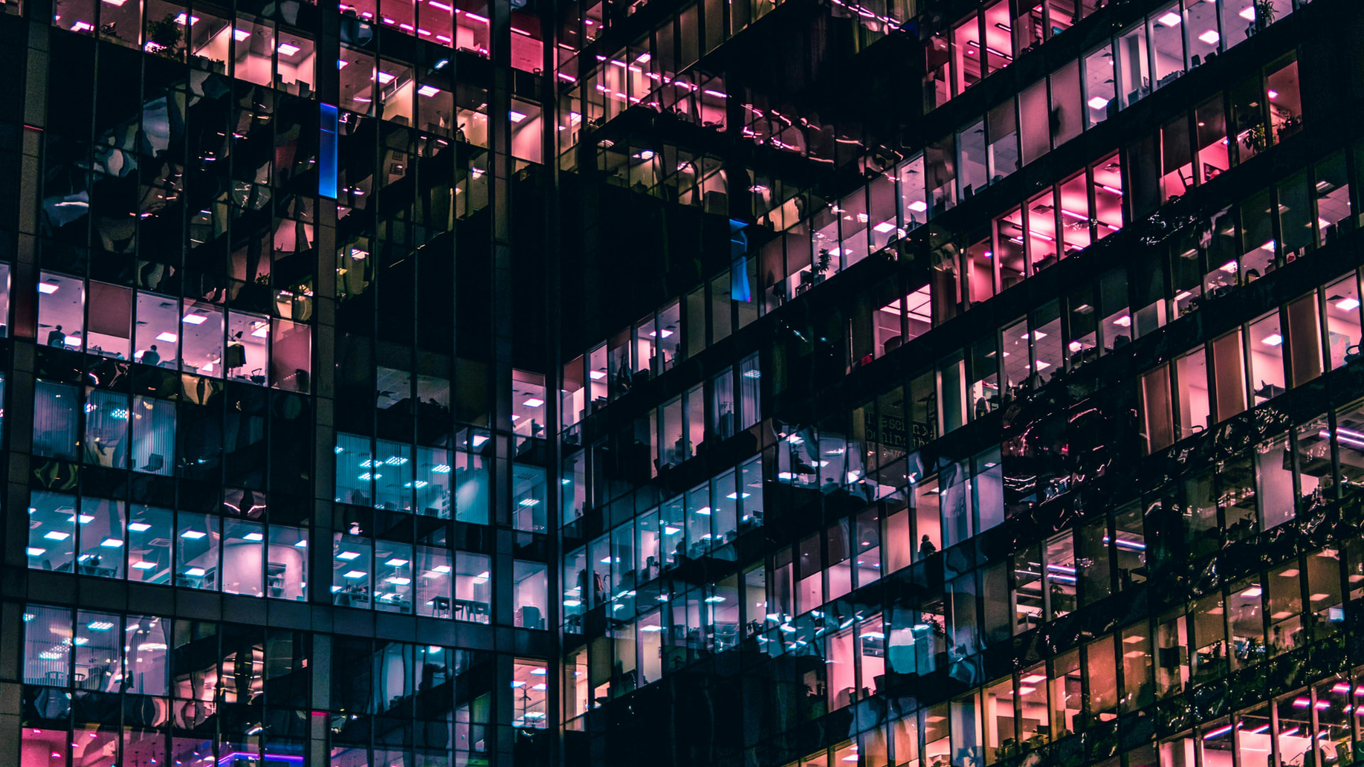 Glass office tower at night glowing with pink and blue lit interiors